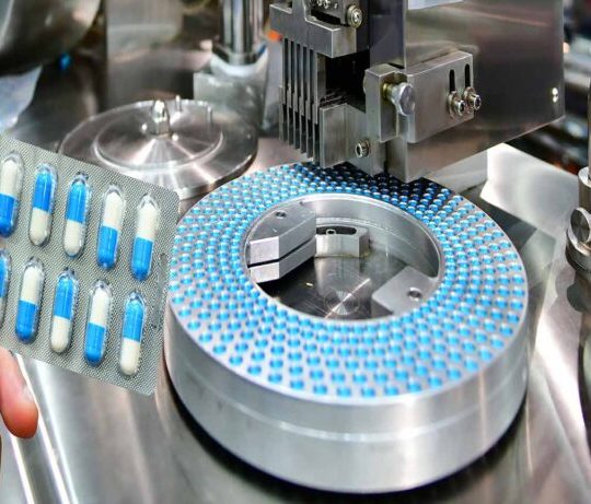 Hand holding blue capsule pack at medicine pill production line,